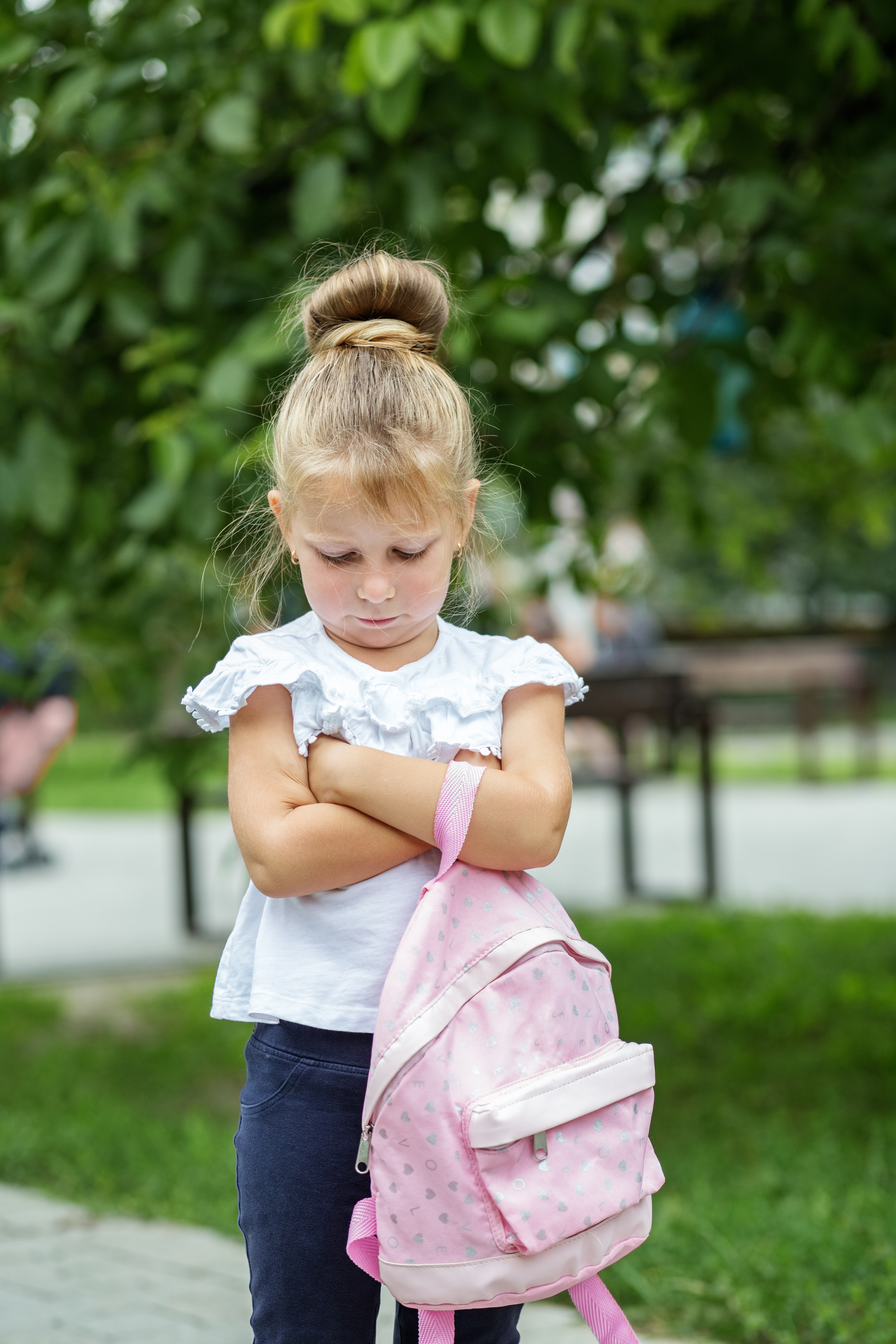 young girl standing on sidewalk with her arms crossed and looking down sadly