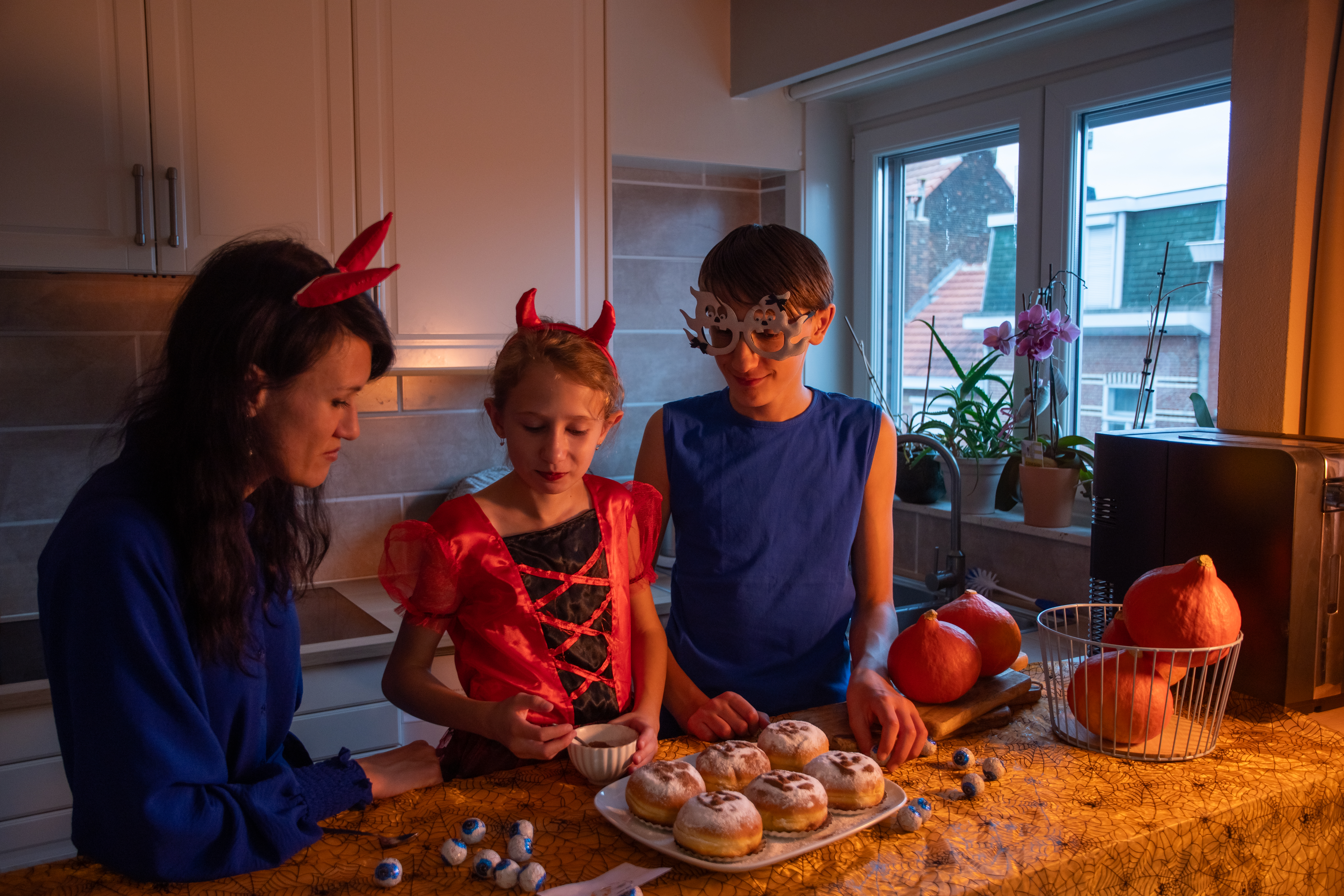 mother, daughter, and son in halloween costumes decorating donuts