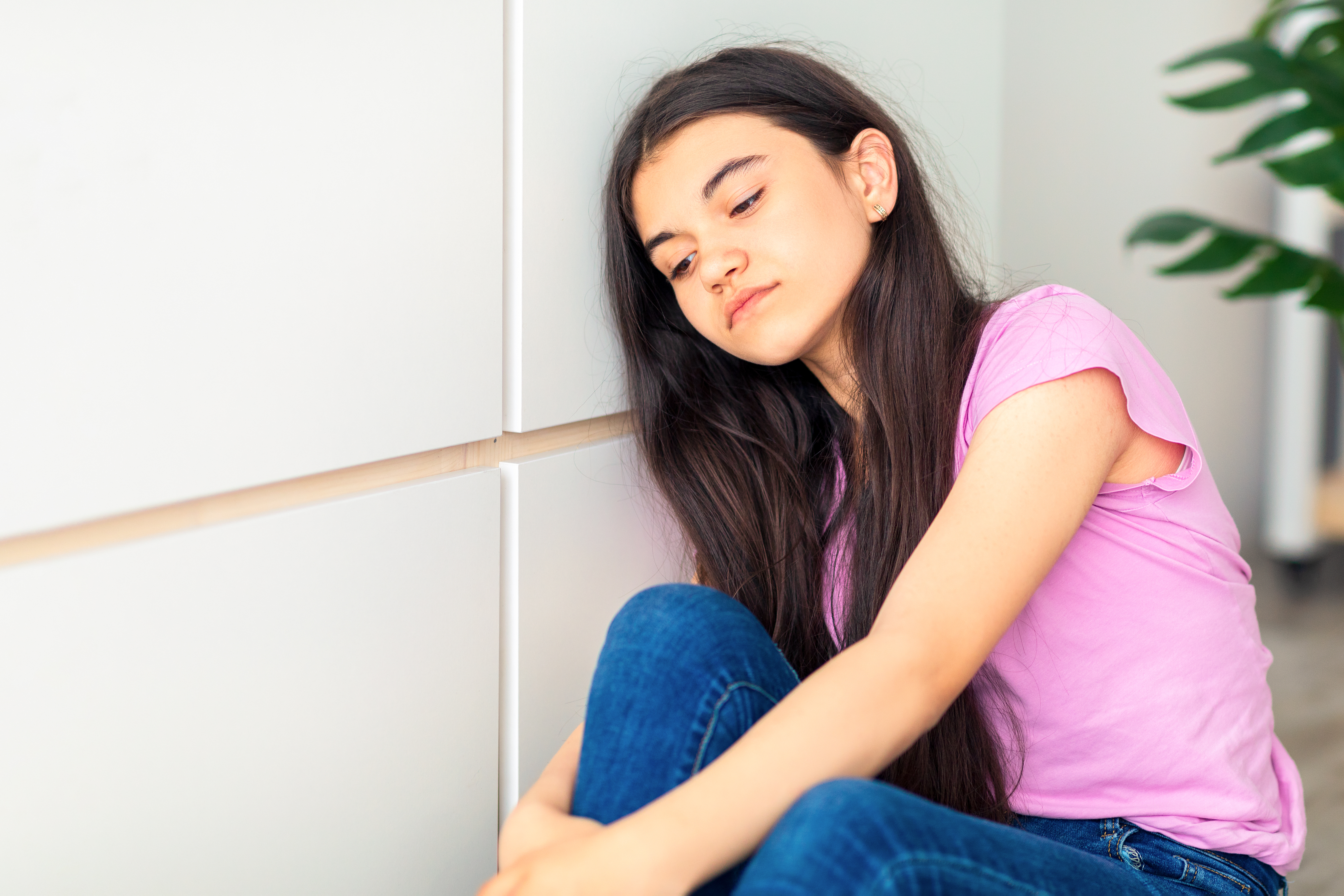 teen girl sitting on the floor, leaning against the wall and looking down