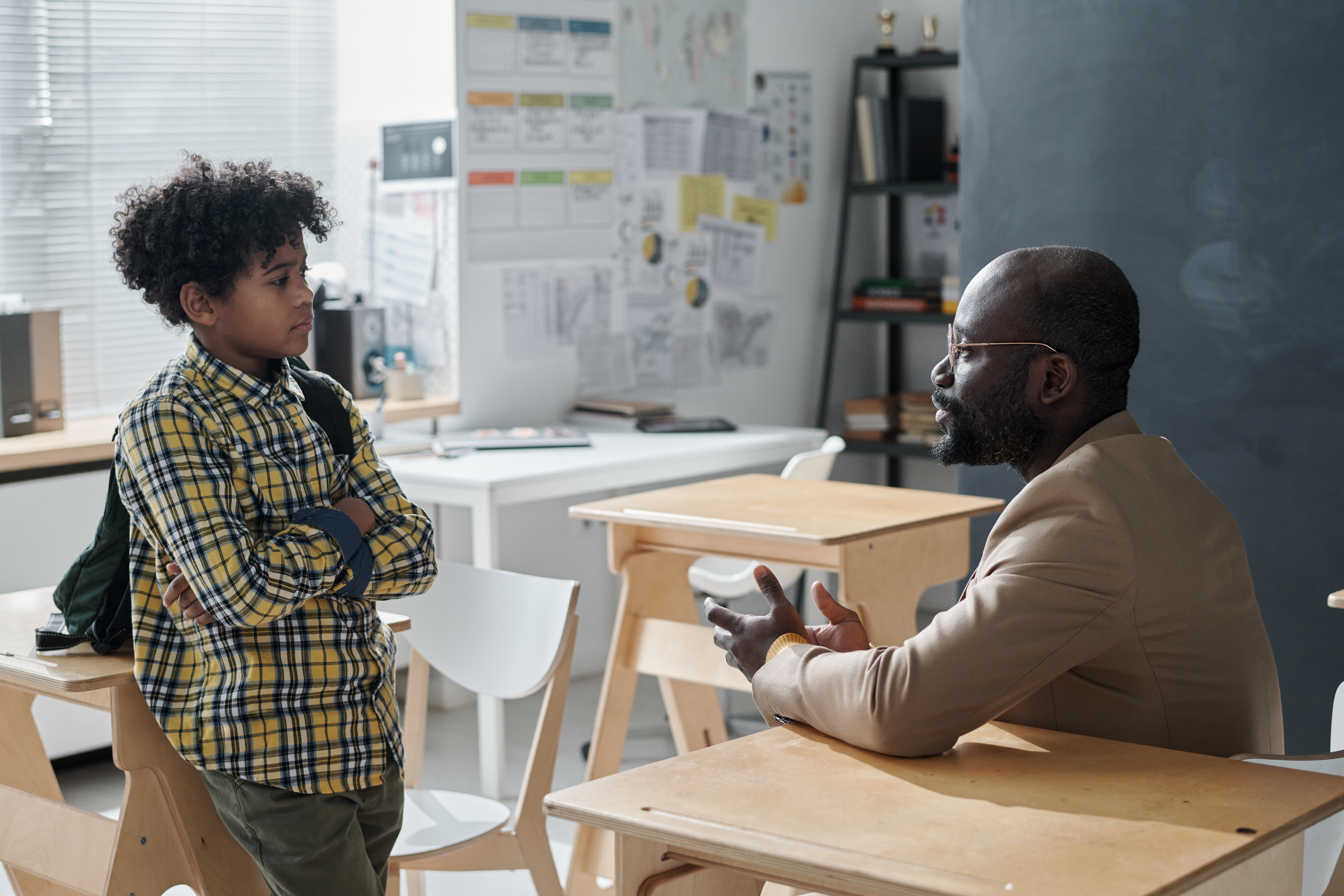 young boy crossing his arms and talking to a teacher in a classroom