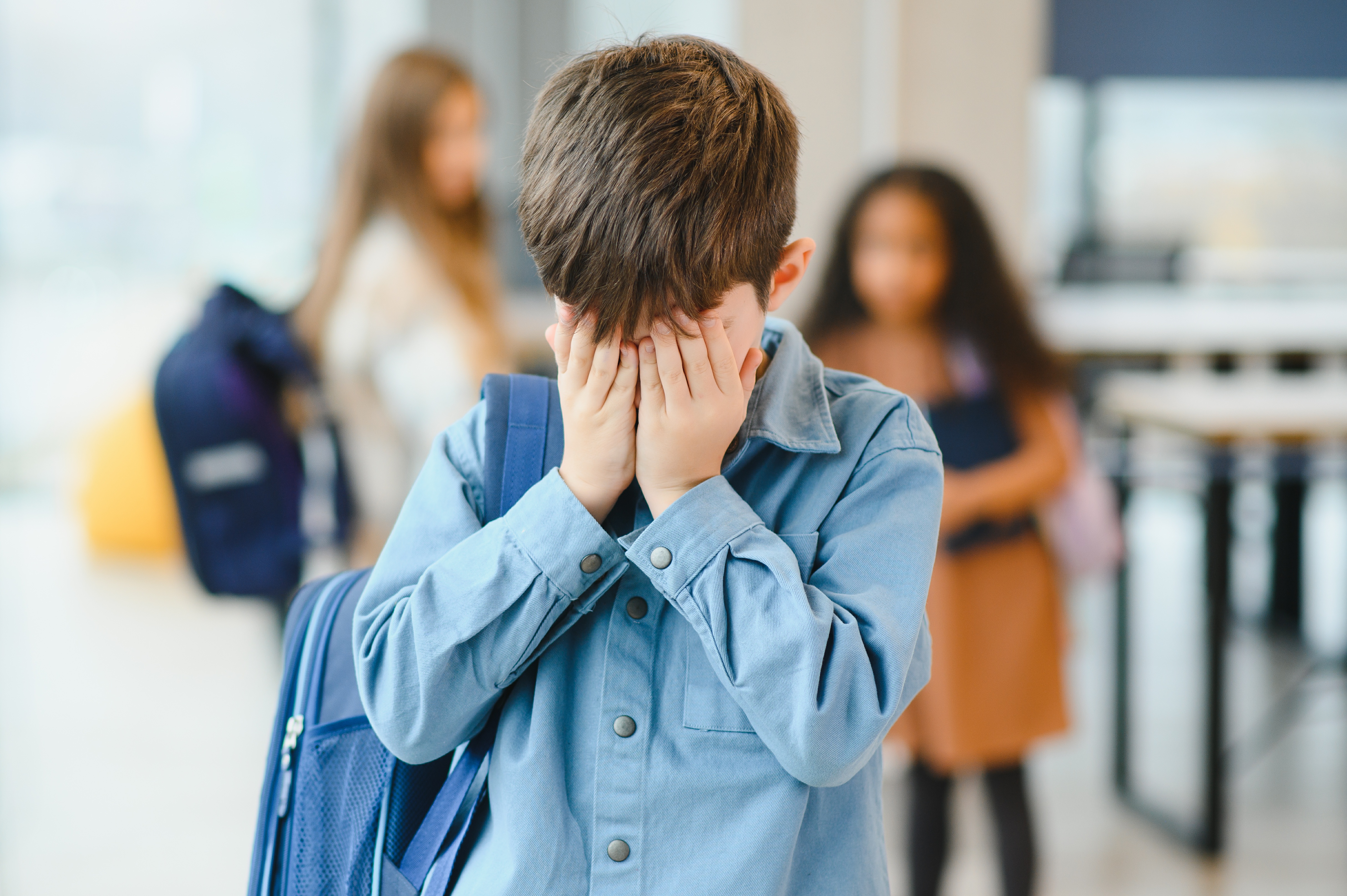 upset boy at school covering his dace with his hands