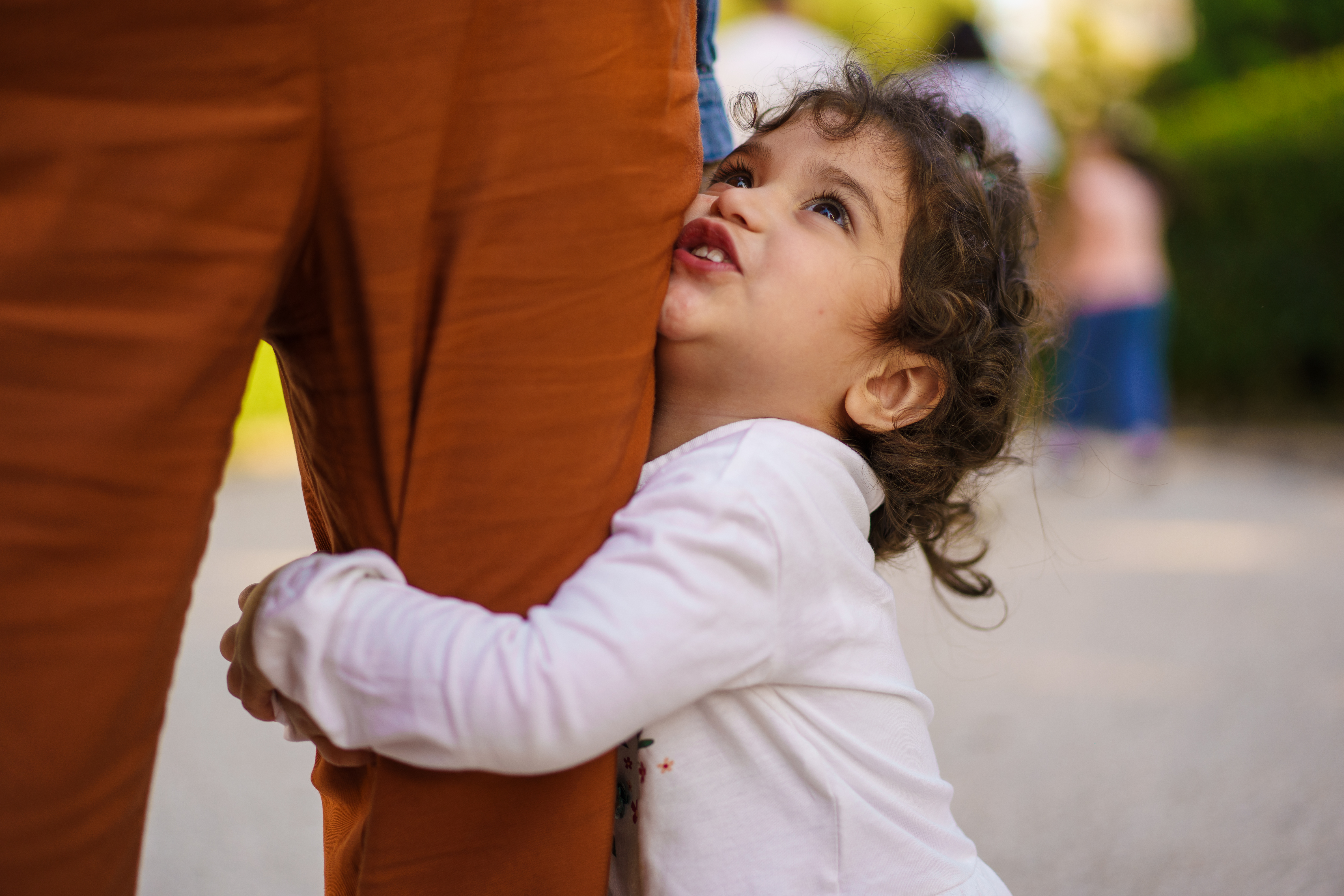 toddler girl hugging the leg of her parent